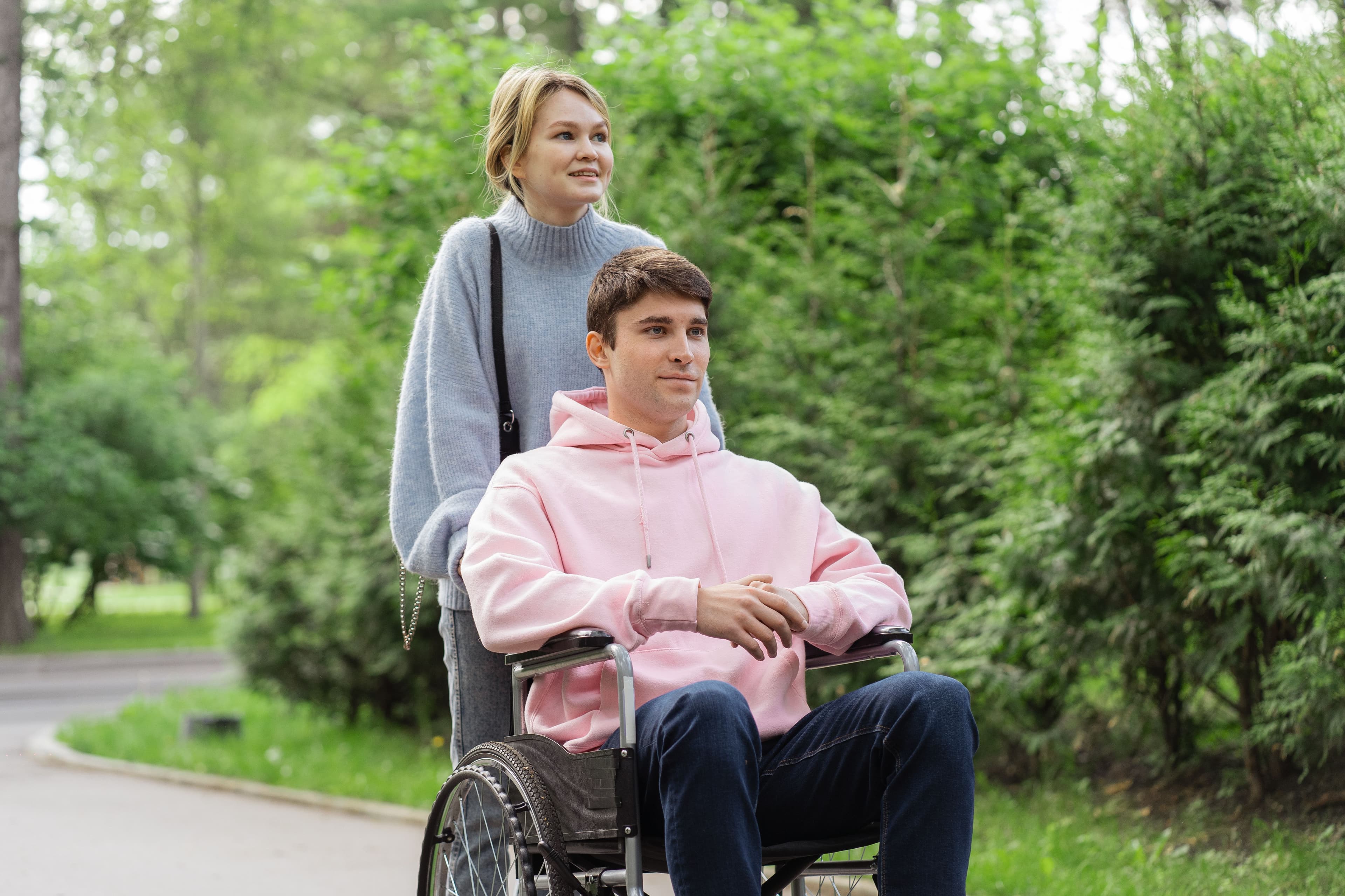 Caregiver walking with a client in a wheelchair through a park